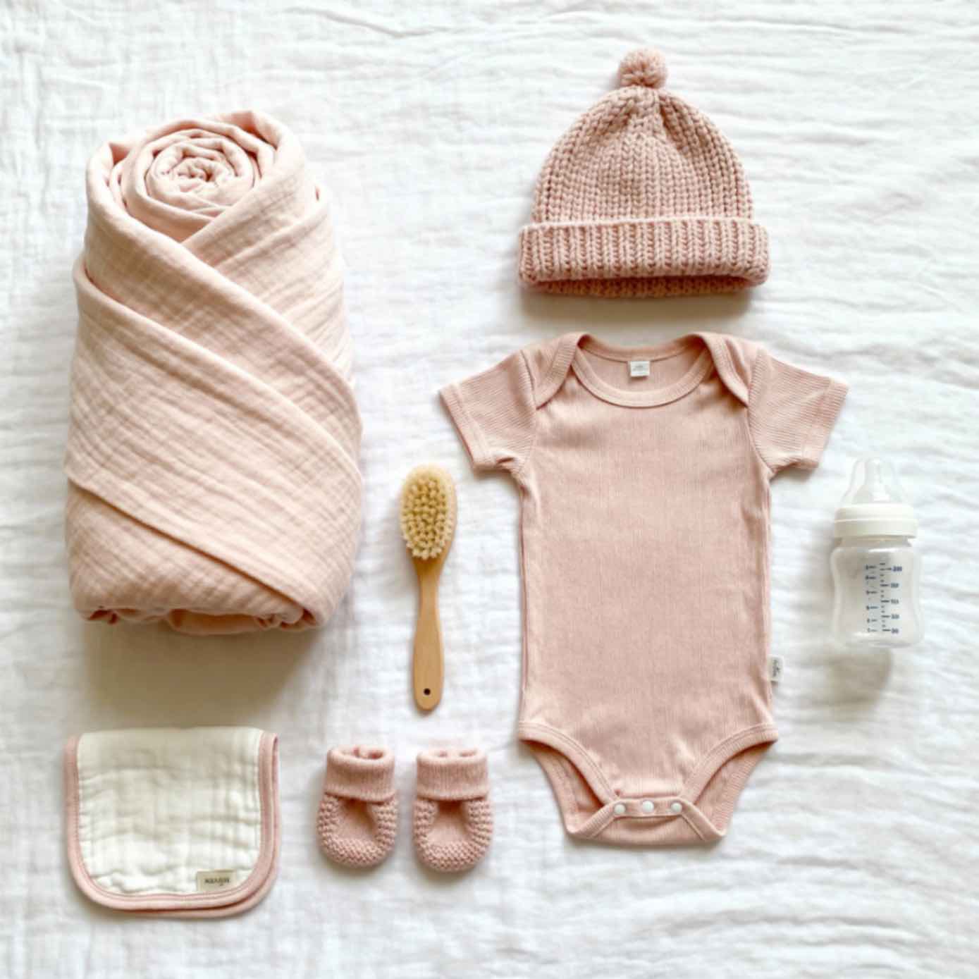 Newborn essentials including soft blankets, onesies, plush toys, and skincare products in a cozy nursery setting.