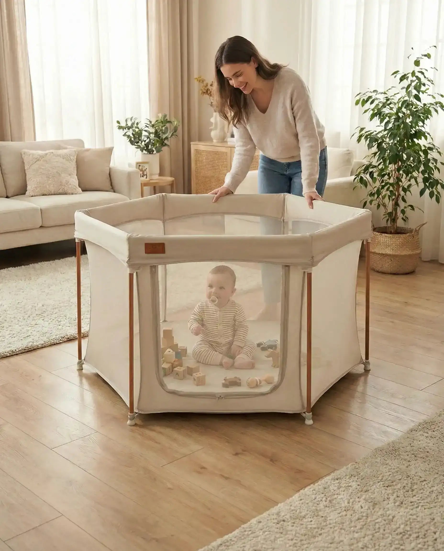 All Stars JOY Baby Playpen Natural Edition by Venture. Woman setting up a portable playpen for a baby in a living room.