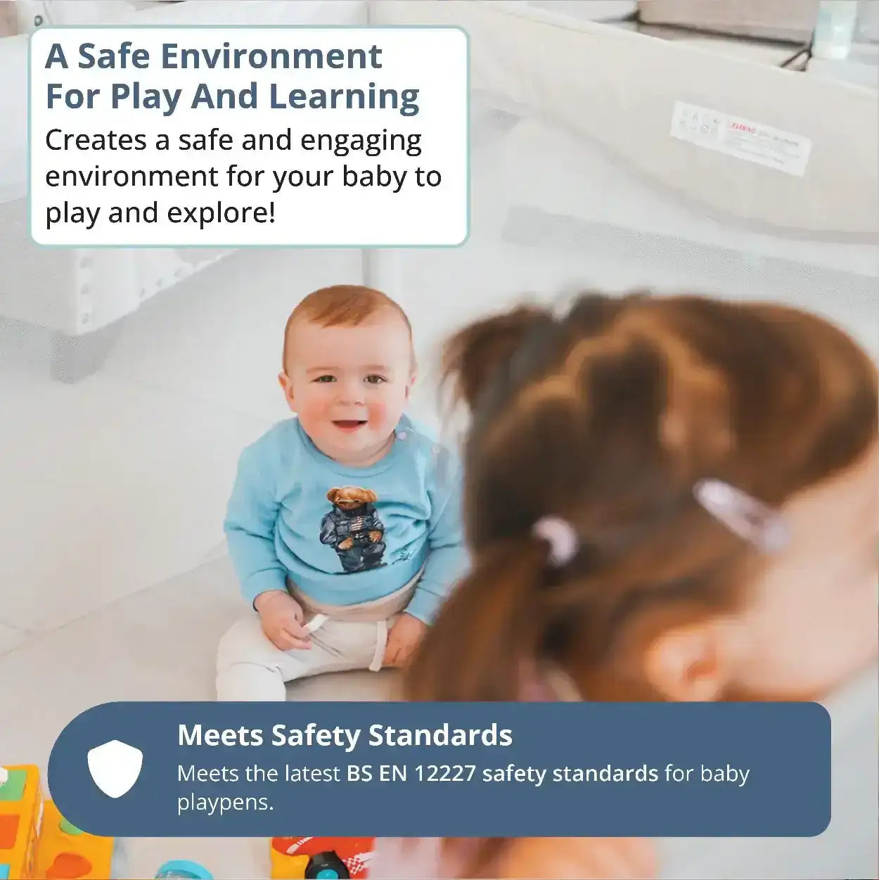 Baby in a blue shirt with a bear design sitting on a playpen, surrounded by toys and text about safety standards. All Stars JOY Baby Playpen by Venture