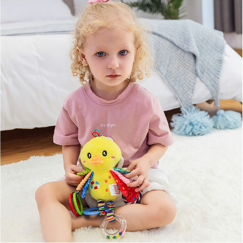 Child holding a colorful toy duck with beads, sitting on a white rug. Baby Stroller & Crib Toy Hanging Plush Sensory Animals bleu ribbon