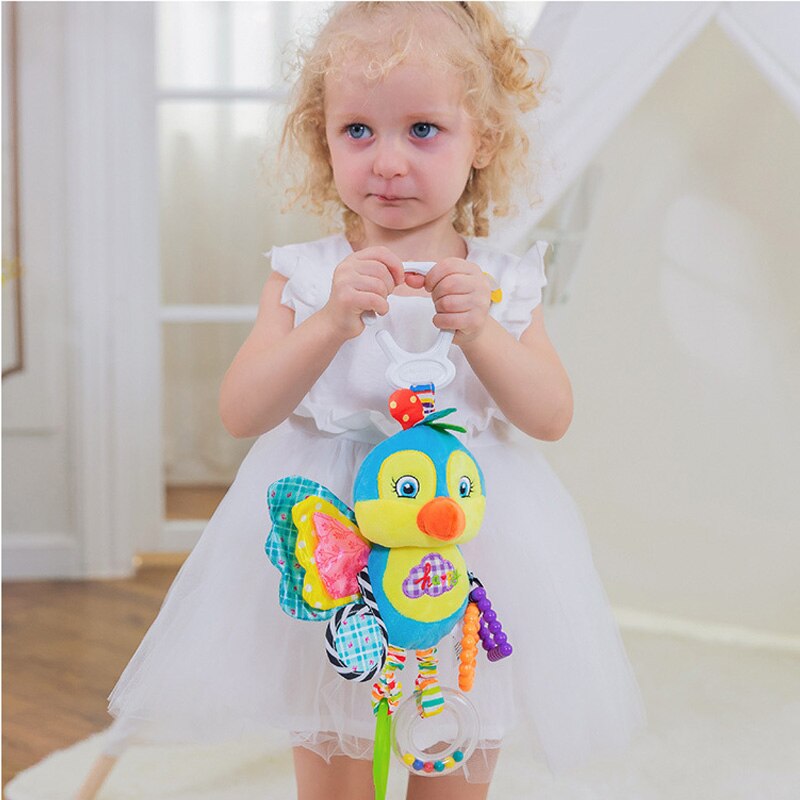 Child holding a colorful butterfly toy indoors. Baby Stroller & Crib Toy Hanging Plush Sensory Animals bleu ribbon