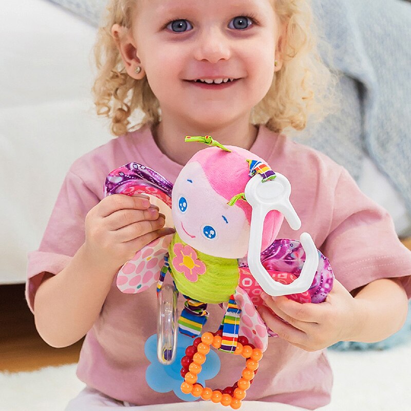 Child holding a colorful baby toy with a soft plush figure and rattle components. Baby Stroller & Crib Toy Hanging Plush Sensory Animals bleu ribbon