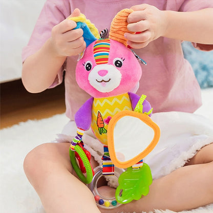 Child holding a colorful plush toy with various textures and attachments. Baby Stroller & Crib Toy Hanging Plush Sensory Animals bleu ribbon