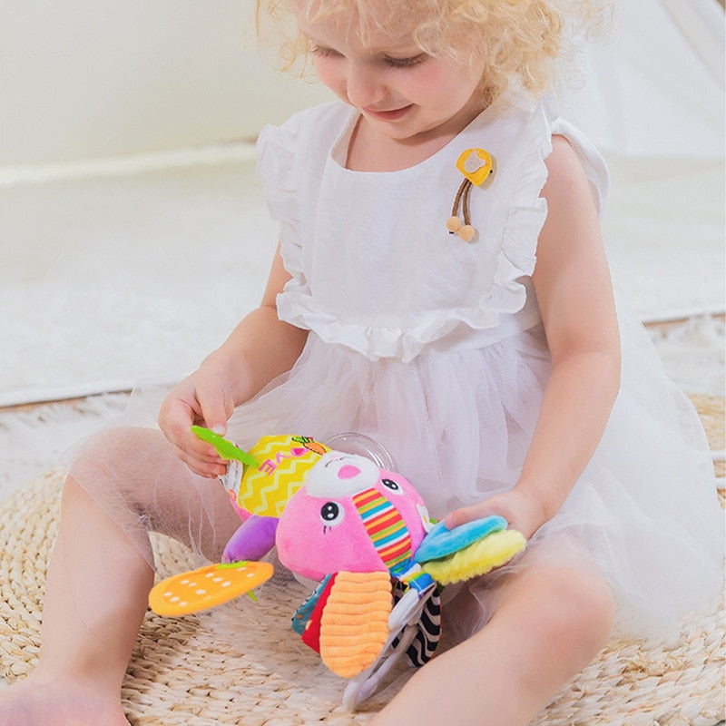 Child playing with a colorful toy on a wooden floor Baby Stroller & Crib Toy Hanging Plush Sensory Animals bleu ribbon