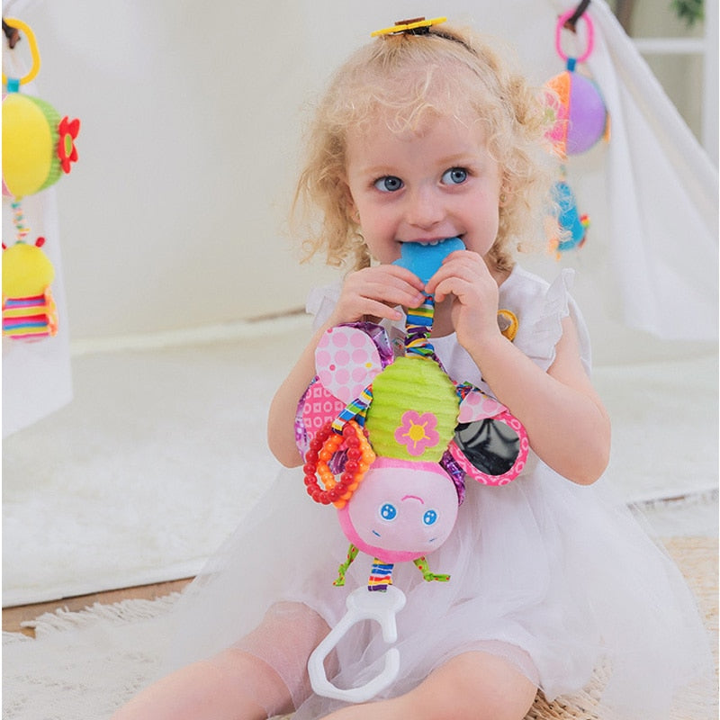 Child holding a colorful baby teether toy indoors. Baby Stroller & Crib Toy Hanging Plush Sensory Animals bleu ribbon