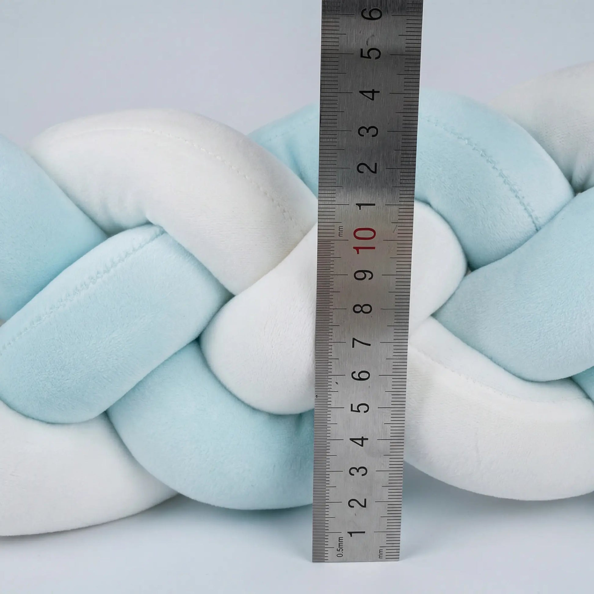 Braided pillow with a ruler for scale on a light blue background. Braided pillow with a ruler for scale on a neutral background  4 Strand Nursery bleu ribbon baby