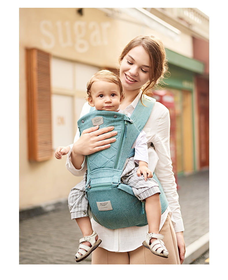 Woman carrying a child in a blue baby carrier on a street. Easy-On Baby Carrier SwiftWear Ergonomic Infant Carrier for Dads Moms bleu ribbon