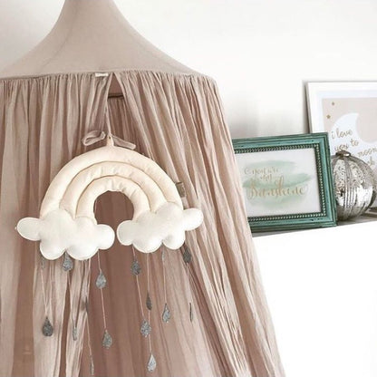Decorative cloud and rainbow mobile hanging from a canopy bed with a blurred background. bleu ribbon