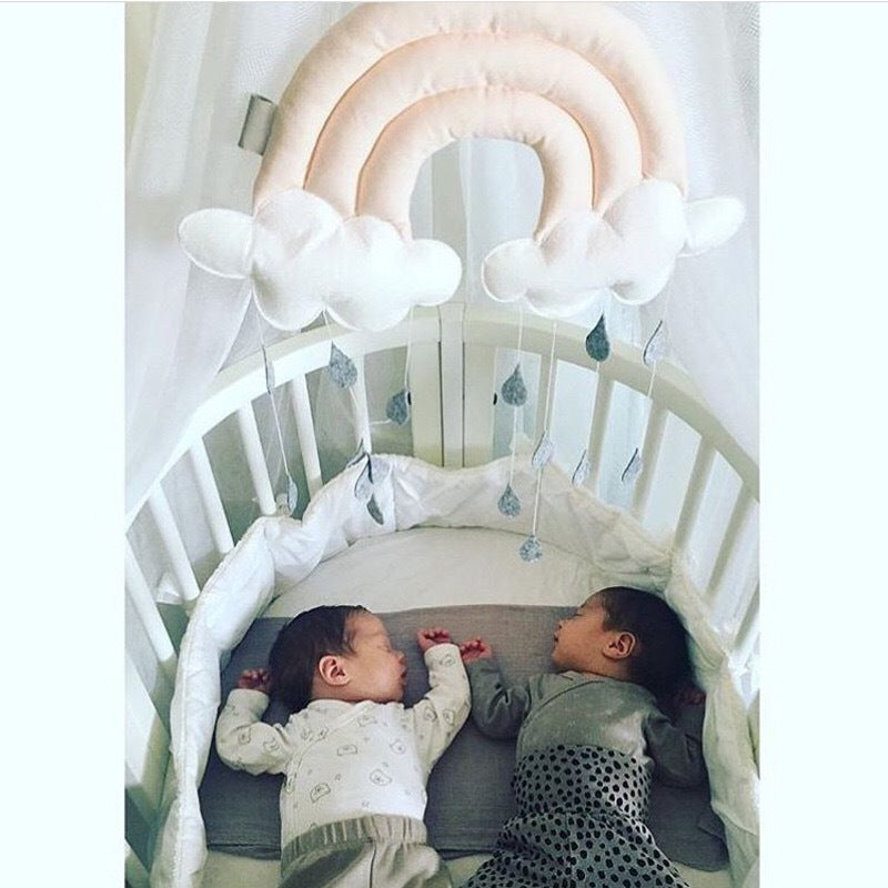 Two babies lying in a crib with a decorative cloud arch above them. bleu ribbon