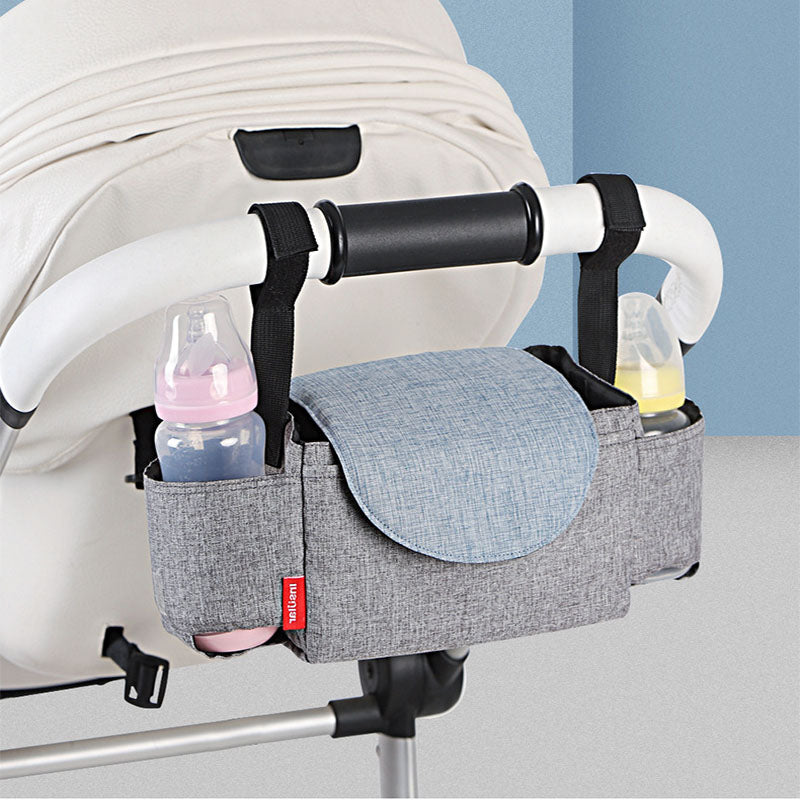 Gray stroller organizer with bottles attached to a stroller against a light blue wall. bleu ribbon