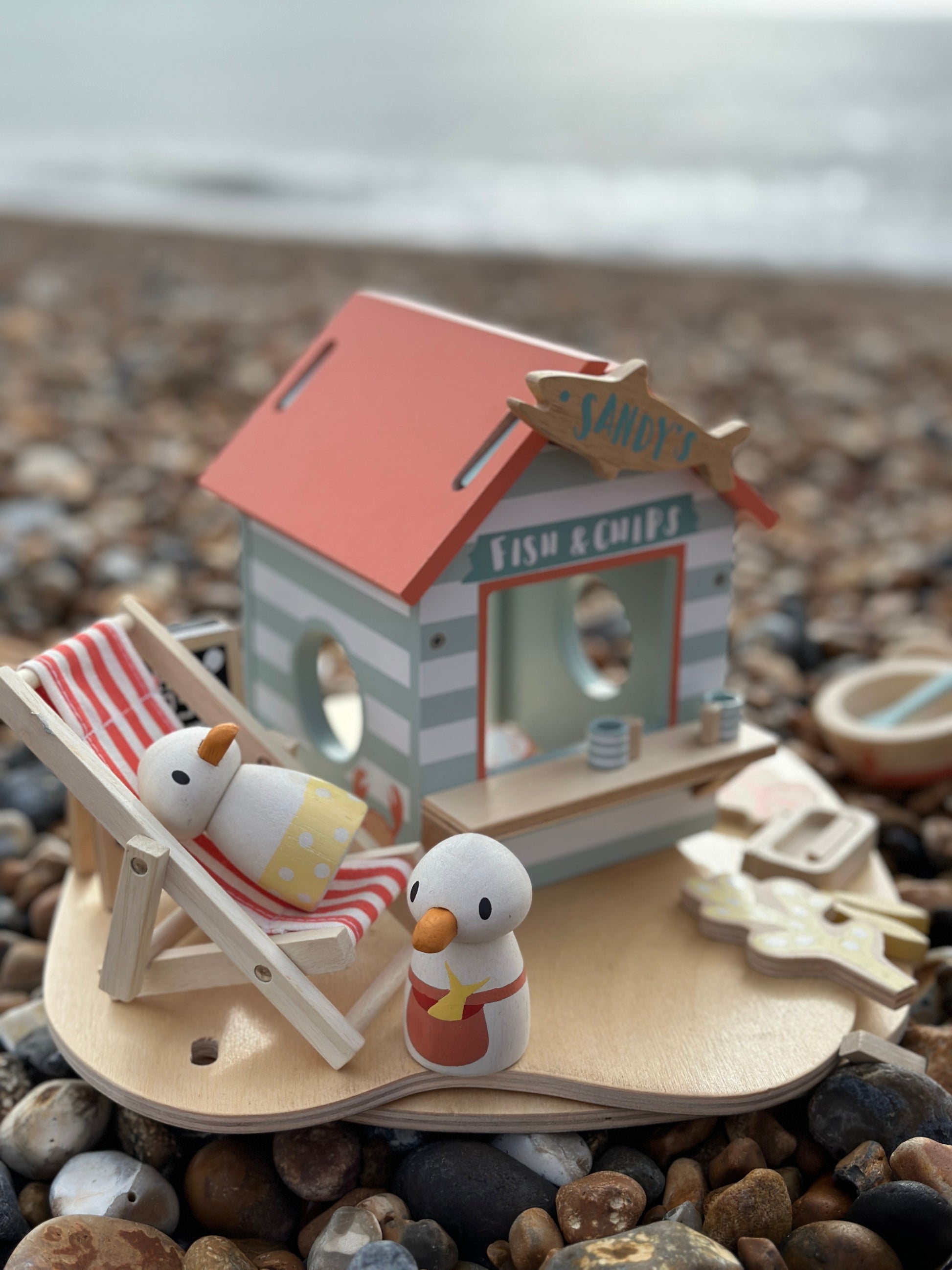 Miniature fish and chip shop with snowman figures on a pebble beach. Sandy's Beach Hut by Tender Leaf Toys - Wooden fish and chips stall set