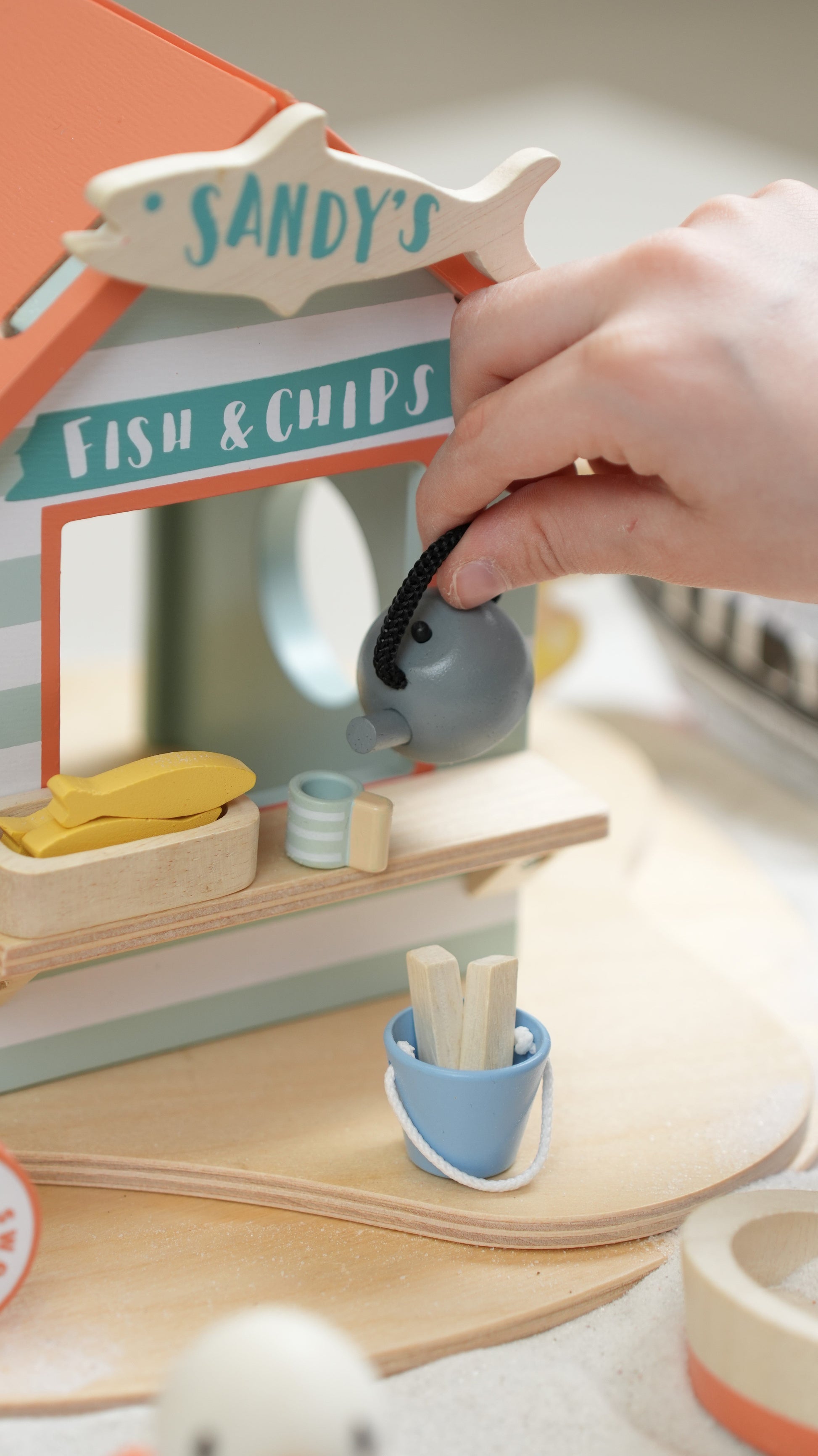Wooden toy fish and chip shop with a hand interacting with it. Sandy's Beach Hut by Tender Leaf Toys - Wooden fish and chips stall set