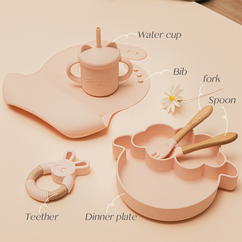 Baby feeding set with water cup, bib, fork, spoon, teether, and dinner plate on a beige background. bleu ribbon