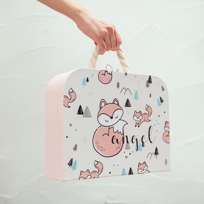 Suitcase with fox design and 'angel' text held by a hand on a light background bleu ribbon baby