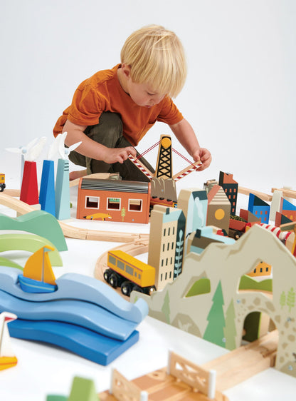 Child playing with a wooden toy train set on a white surface Mountain View Wooden Train Set 58-piece set by Tender Leaf Toys