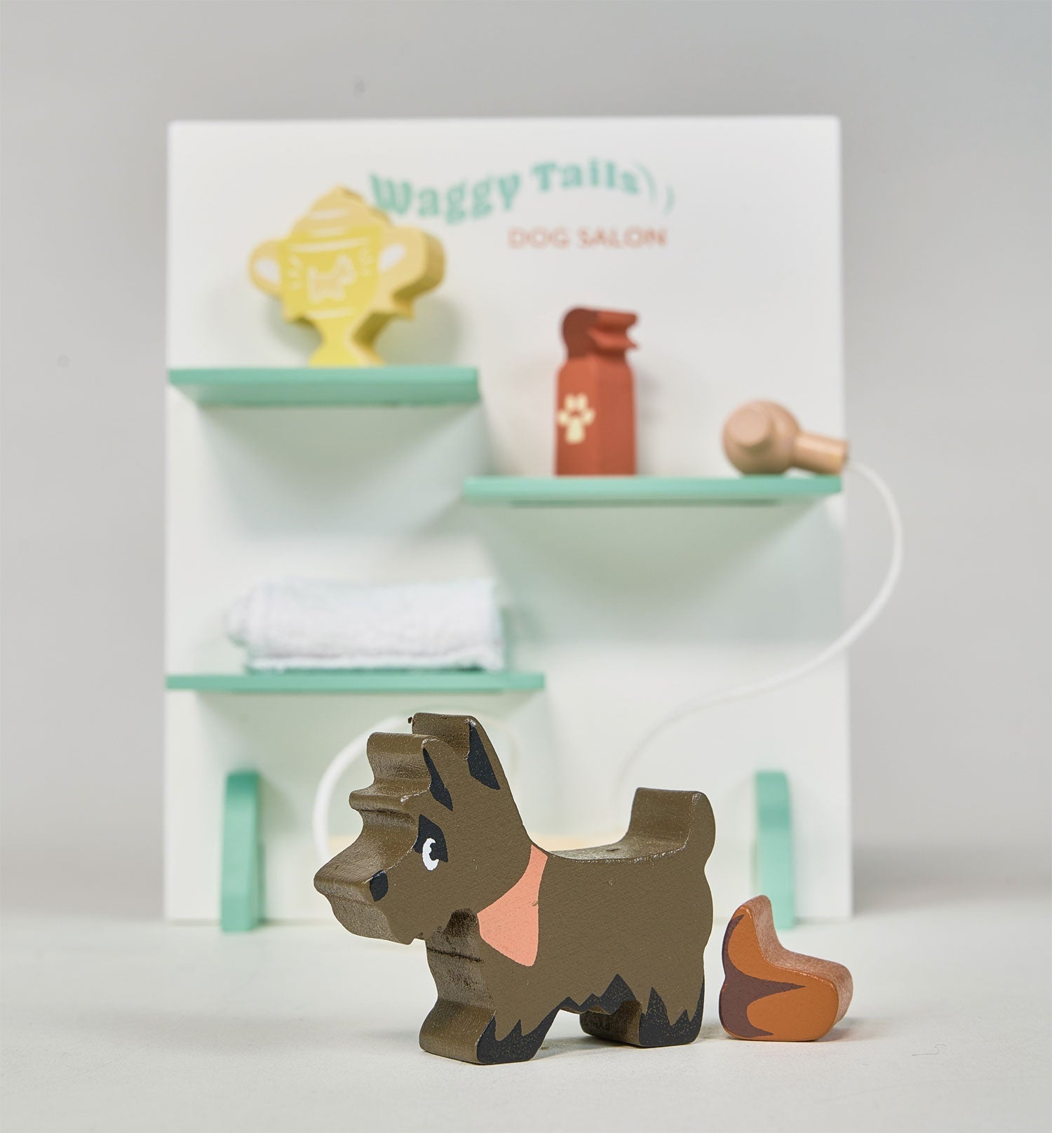 Wooden dog toy in front of a miniature dog salon set on a white background. Waggy Tails Dog Salon by Tender Leaf Toys - Wooden dog grooming set with 7 breeds