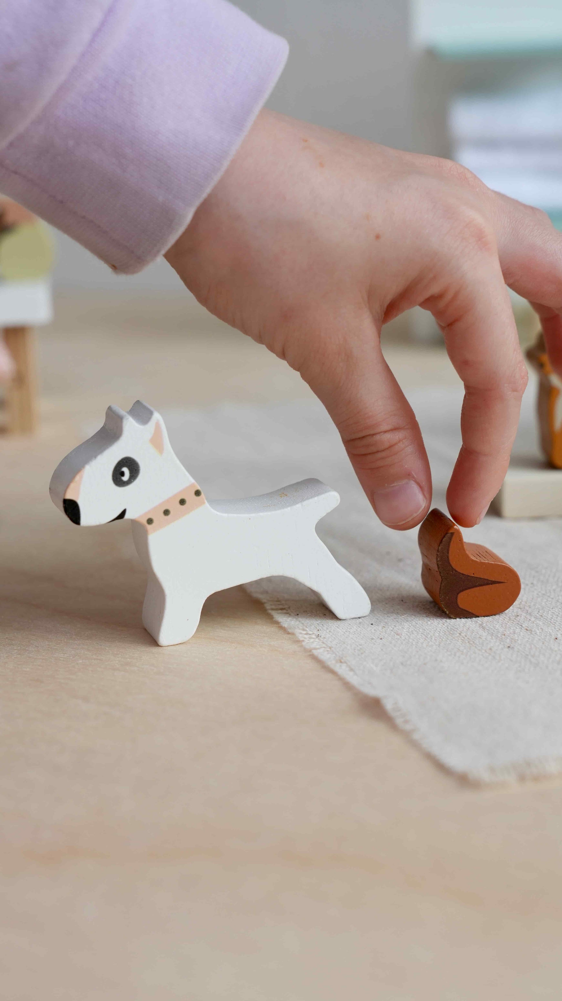 Hand interacting with a small wooden dog figurine on a light surface. Waggy Tails Dog Salon by Tender Leaf Toys - Wooden dog grooming set with 7 breeds