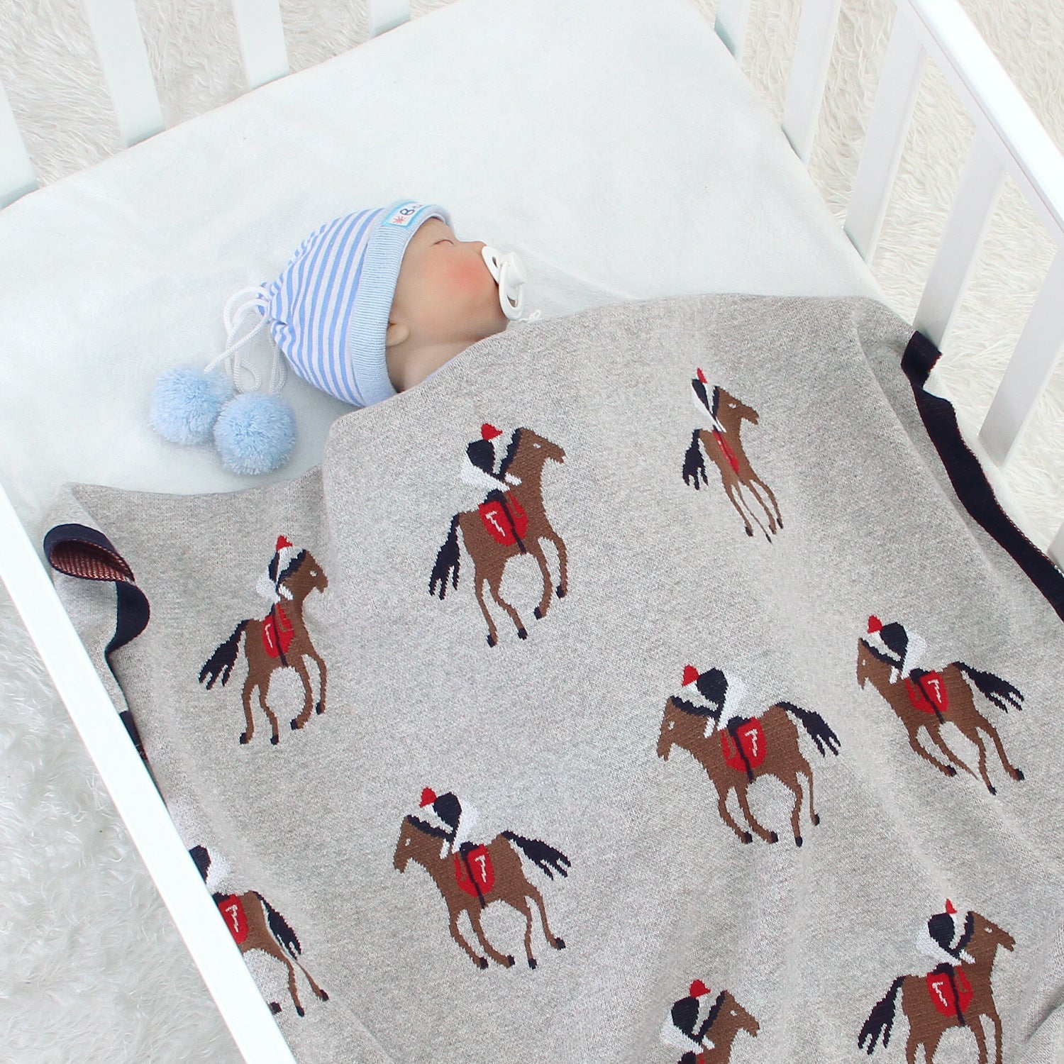 Baby lying on a blanket with horse patterns in a crib bleu ribbon