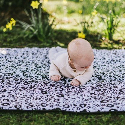 A baby practicing tummy time and developing neck strength on the visually stimulating Etta Loves x Liberty outdoor playmat outdoors among spring flowers.