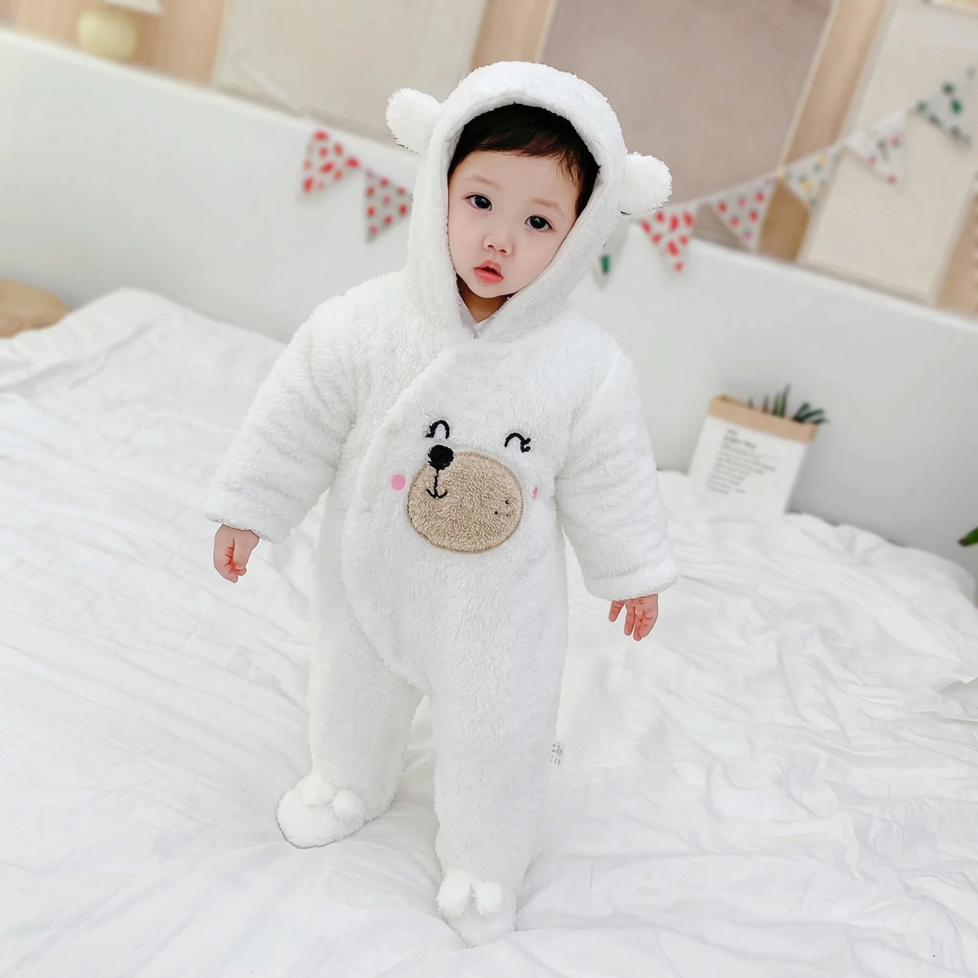 BleuRibbon Baby Winter Jumpsuit – Shu Cotton Velvet Romper​. Baby in a white bear onesie sitting on a bed