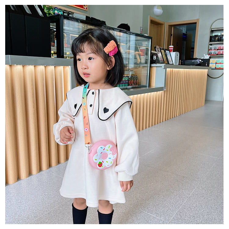 Young girl in a white dress with a colorful bag in a room with wooden paneling. bleu ribbon
