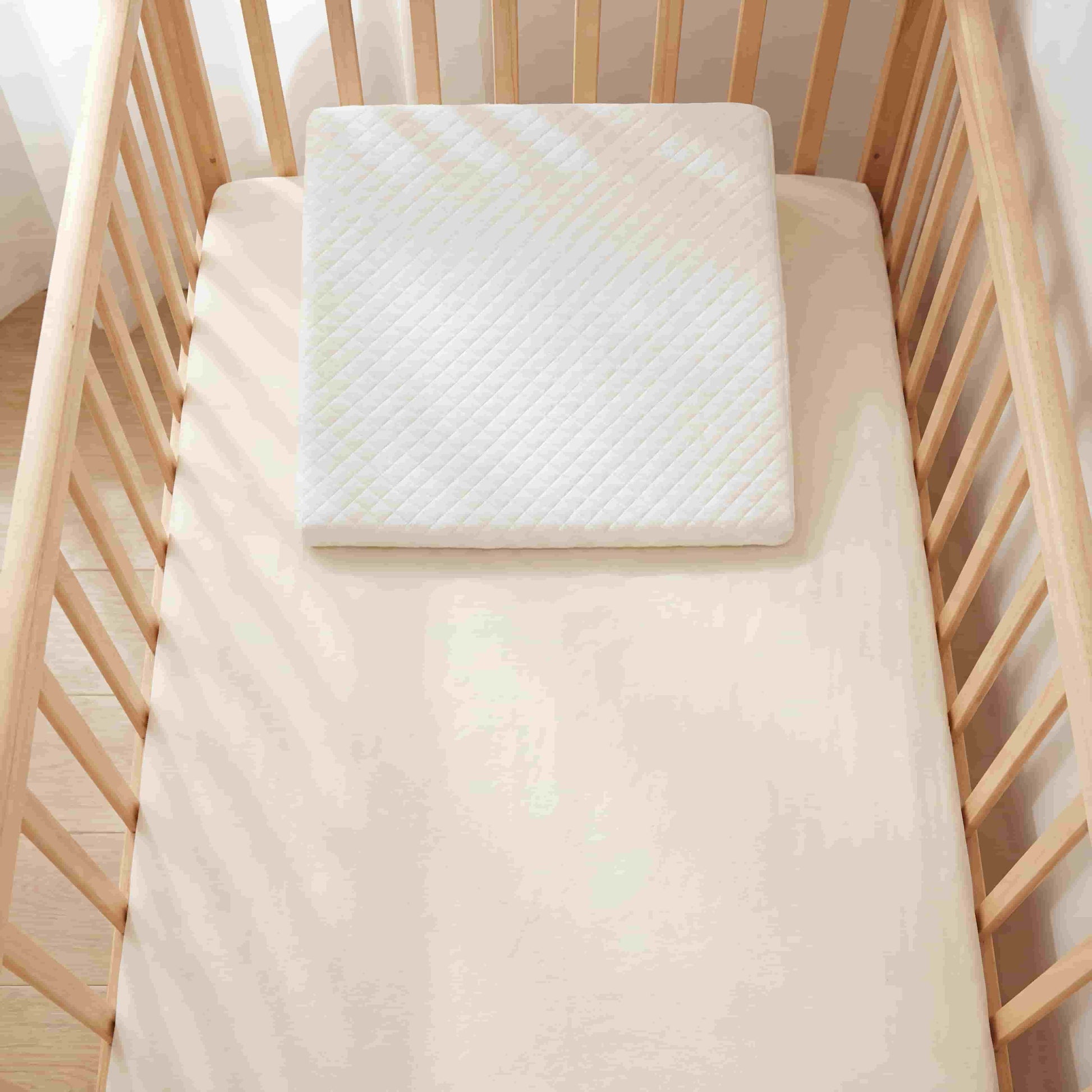 Top-down view of BleuRibbon memory foam wedge pillow placed inside a standard baby crib. Universal fit design for cribs and bassinets to help babies sleep better.