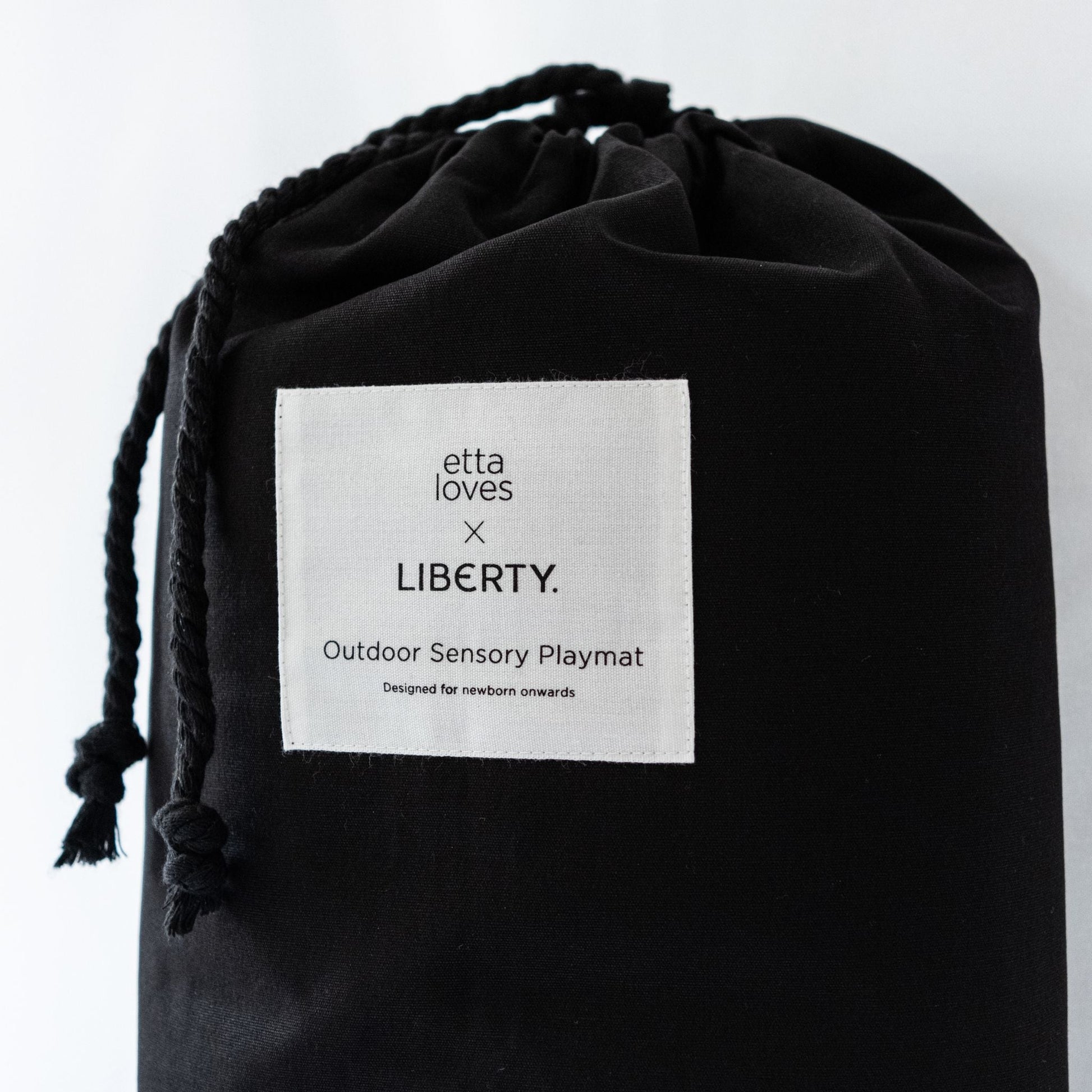 The premium black canvas drawstring carry bag featuring the Etta Loves x Liberty London co-branded label, designed for easy travel with the outdoor playmat.