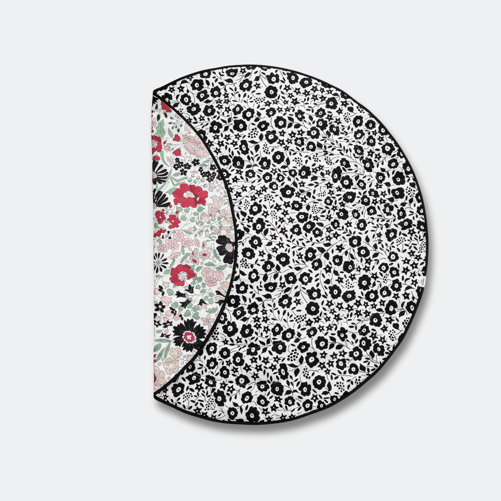 Folded Etta Loves x Liberty round reversible sensory playmat showing both the black and white Fairford Shadow and colorful Wharfedale Meadow patterns.