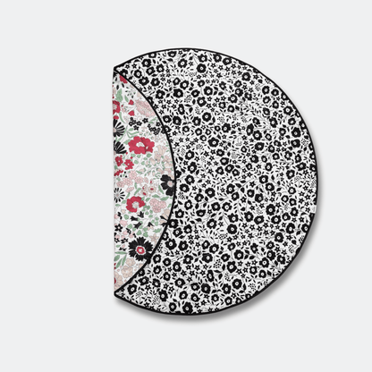 Folded Etta Loves x Liberty round reversible sensory playmat showing both the black and white Fairford Shadow and colorful Wharfedale Meadow patterns.