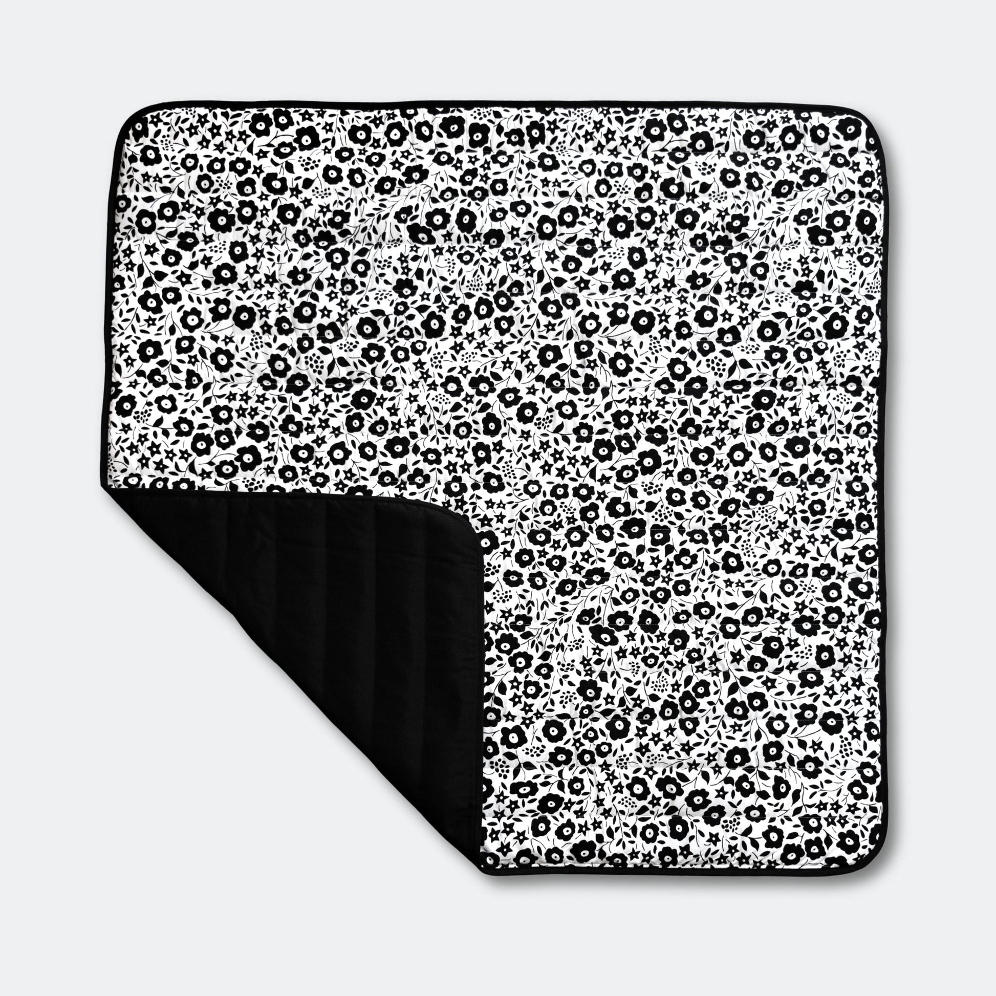 Full top view of the Etta Loves x Liberty outdoor sensory playmat, featuring a folded corner that reveals its practical, water-resistant black base.