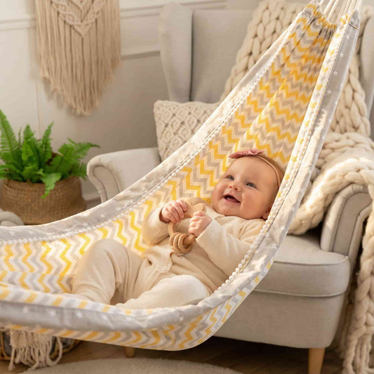 Smiling six-month-old baby lying comfortably inside the Nordic Zen Baby Hammock with yellow chevron pattern, showcasing the secure cocoon design.