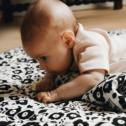 A newborn baby highly engaged and visually focused on the high-contrast black and white Liberty pattern during tummy time.