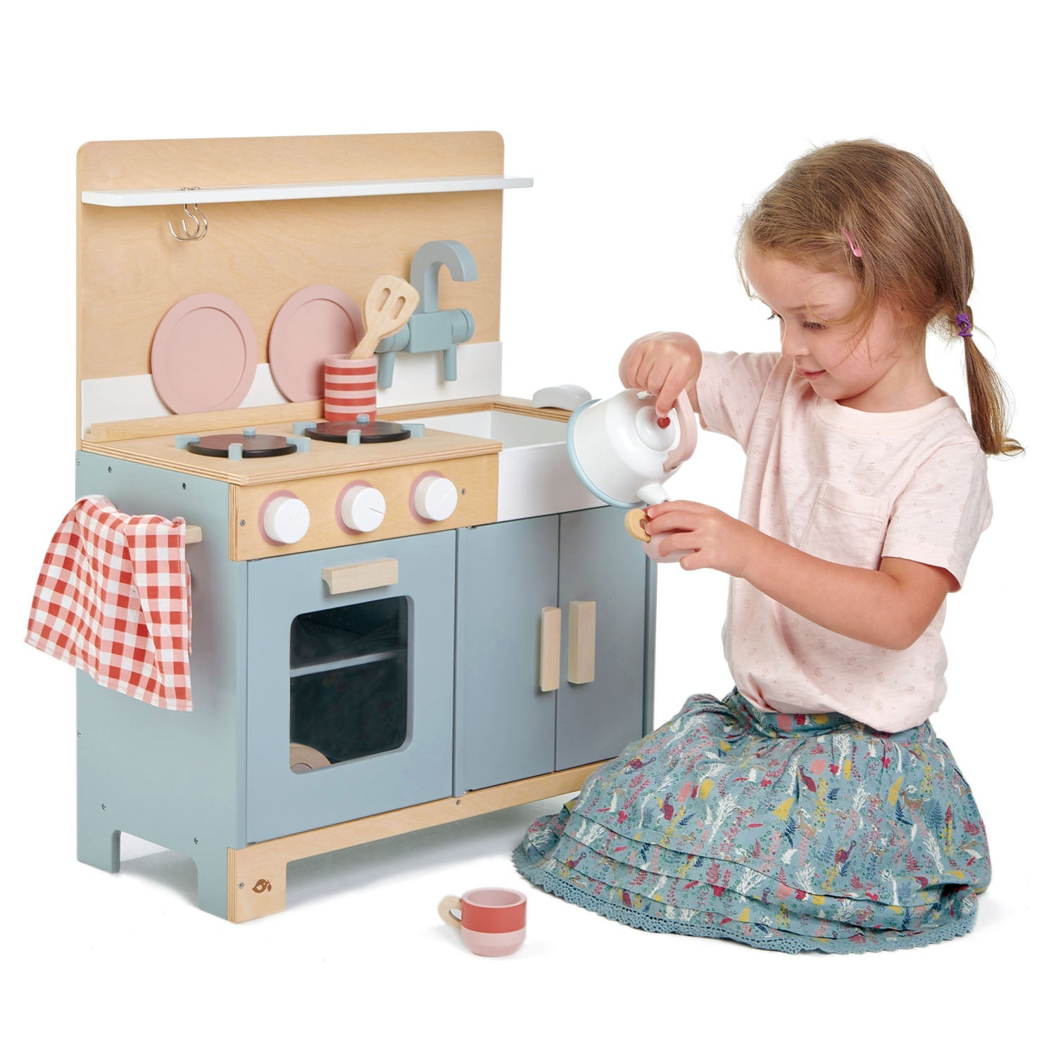 Child playing with a toy kitchen set on a white background A collection of included wooden accessories: a solid white kettle, utensils with holder, and a slicing baguette on an oven tray for creative play.