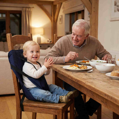Happy baby sitting at a dining table using the BabySafe fabric harness during a family visit, providing a clean and germ-free alternative to shared high chairs.