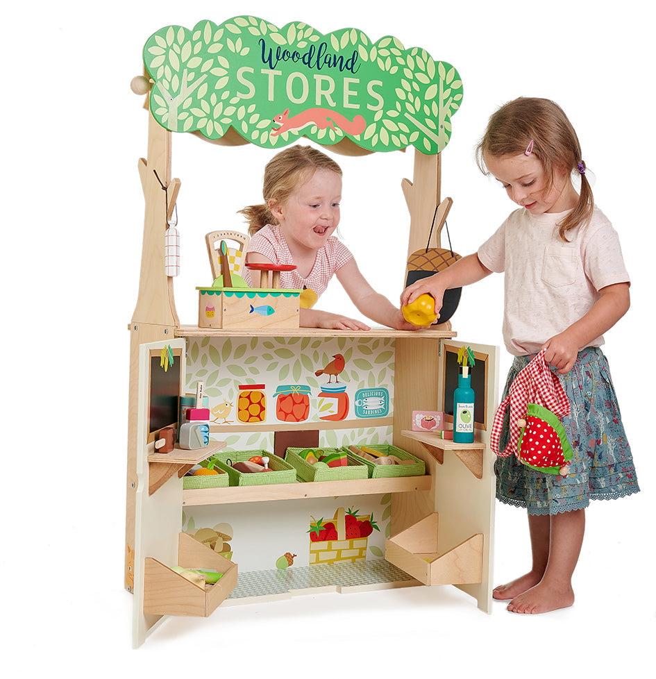 Children playing with a wooden toy store set up with various items on a white background Wooden play shop interior with shelves, strawberry tote bag, and open doors for grocery play.