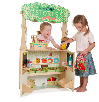 Children playing with a wooden toy store set up with various items on a white background Wooden play shop interior with shelves, strawberry tote bag, and open doors for grocery play.